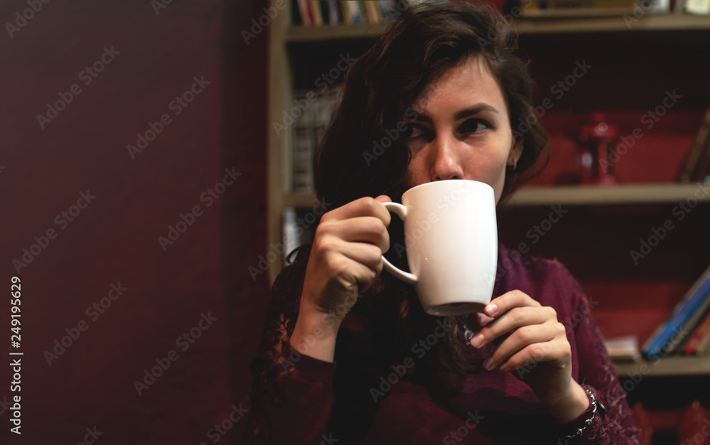 Beautiful Young Woman Drinking Coffee or Tea. Girl Start drinking decaffeinated drinks and enjoying this beverage. Lady holding Cup of coffee or tea over red background with books with space for your