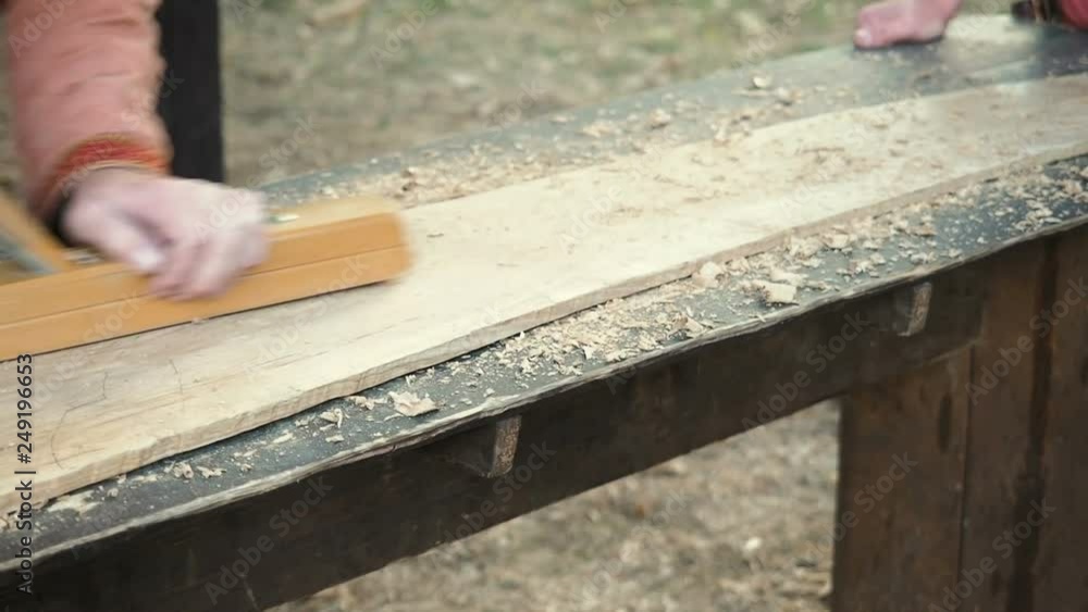 Carpenter in Medieval Cotton Clothes Working With a Wood by Plane. Man Manually Hews a Wooden Board With a Plane Carpenter in Medieval Cotton Clothes Working With a Wood by Plane. Man Manually Hews a Wooden Board With a Plane