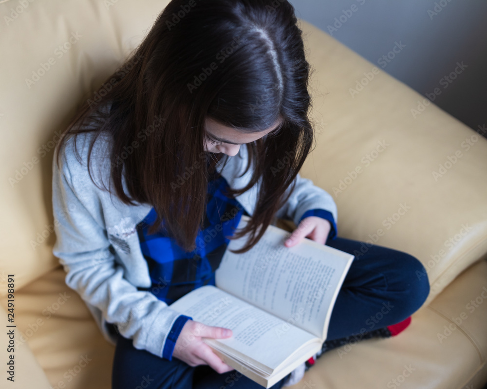 background. beautiful girl reading a book while sitting in a chair in her room background. beautiful girl reading a book while sitting in a chair in her room