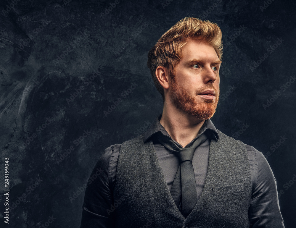 Portrait of a handsome redhead man dressed in elegant vest and tie in studio against a dark textured wall Portrait of a handsome redhead man dressed in elegant vest and tie in studio against a dark textured wall