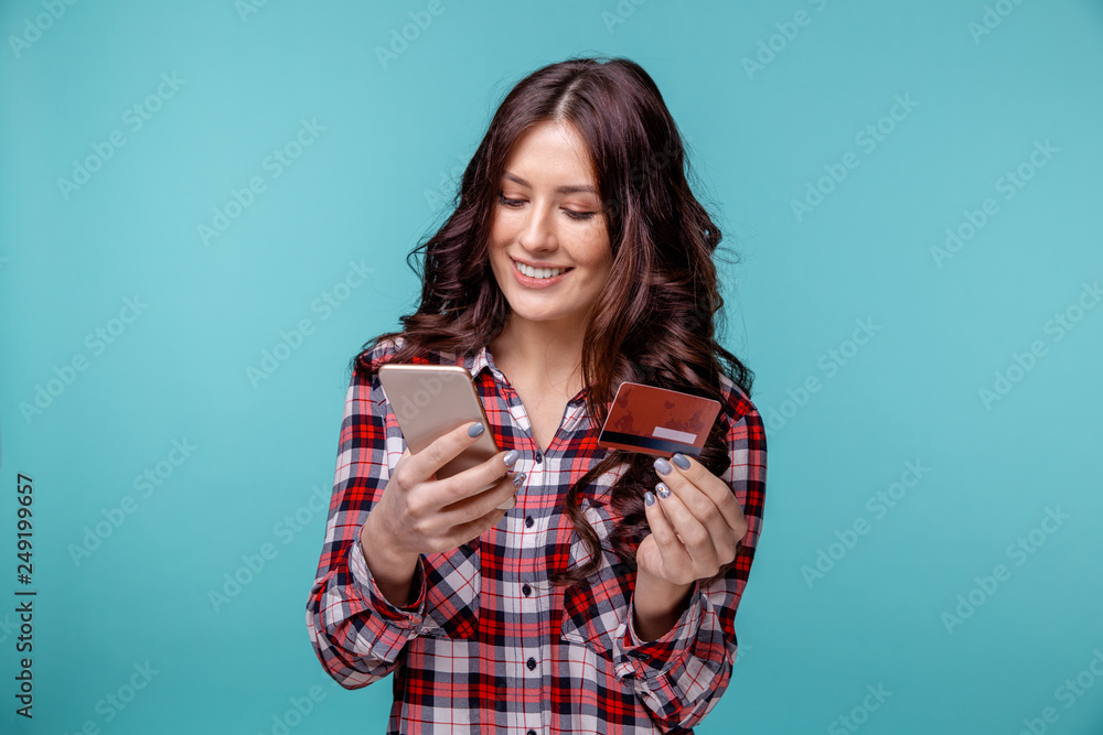 young girl isolated over blue background using mobile phone holding credit card. young girl isolated over blue background using mobile phone holding credit card.
