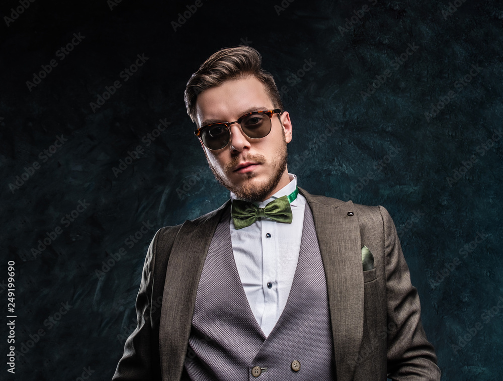 Fototapeta premium A stylish man in sunglasses dressed in an elegant suit against a dark textured wall