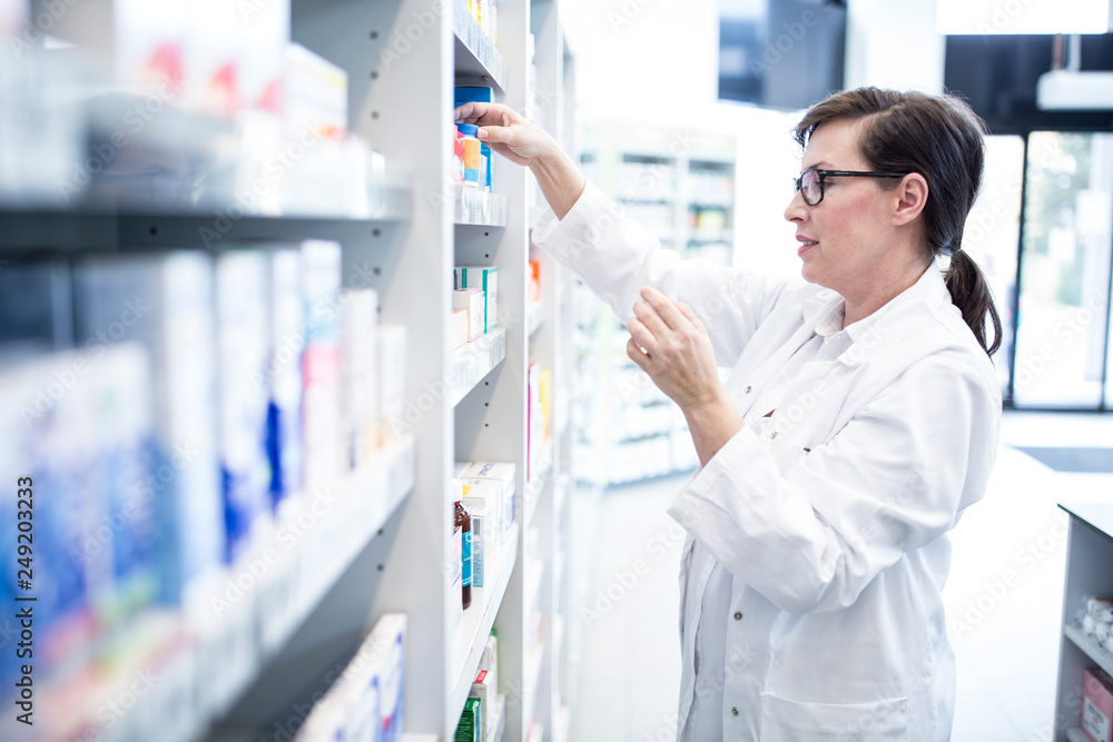 Pharmacist sorting medicine at shelf in pharmacy Pharmacist sorting medicine at shelf in pharmacy