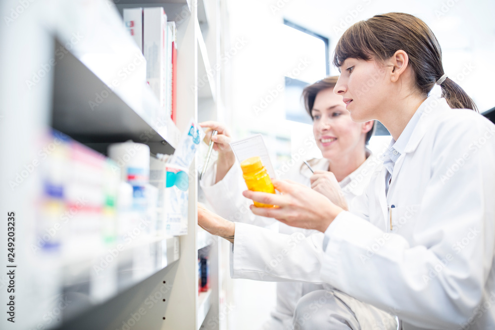 Two pharmacists with pill box at shelf in pharmacy Two pharmacists with pill box at shelf in pharmacy