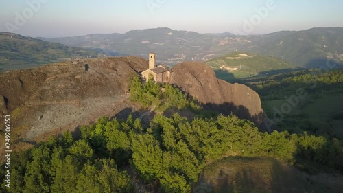 Aerial drone video at sunset time of a small ancien church built into the rocks on the hills of the Trebbia Valley, near Piacenza, Italy.