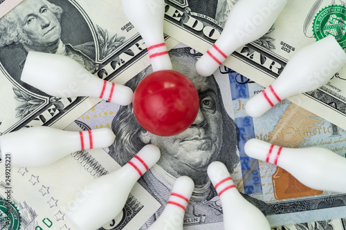 Red winning bowling strike ball surround with knocked down pins on pile of US dollar banknotes money, financial success target concept, goals on investment or profit in stock market concept © Nuthawut
