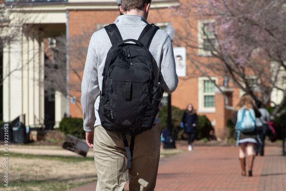 A male college student walks across a college campus A male college student walks across a college campus