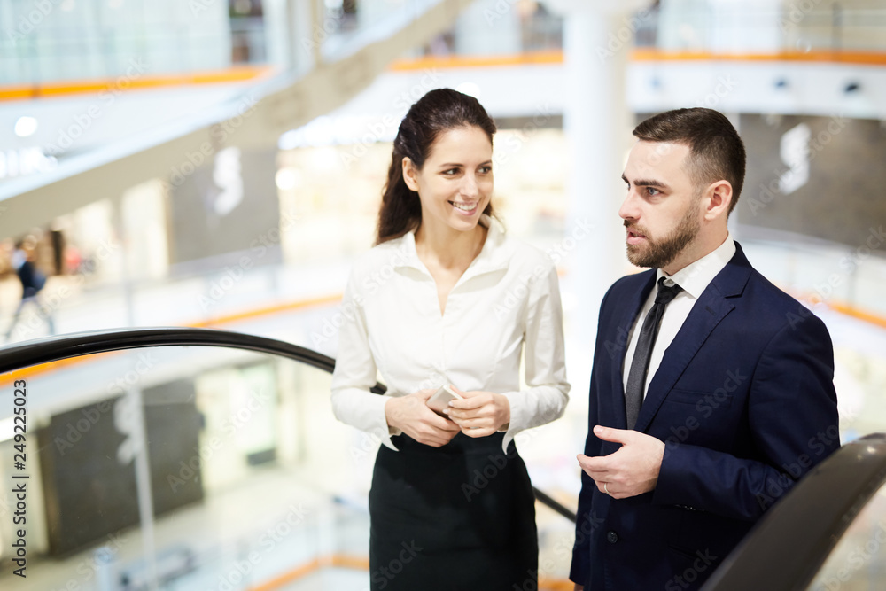 Young elegant businessman discussing news with his colleague while both moving on elevator in the mall Young elegant businessman discussing news with his colleague while both moving on elevator in the mall