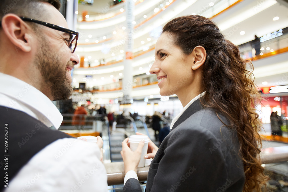 Two happy colleagues in formalwear having drinks at break inside large contemporary mall Two happy colleagues in formalwear having drinks at break inside large contemporary mall