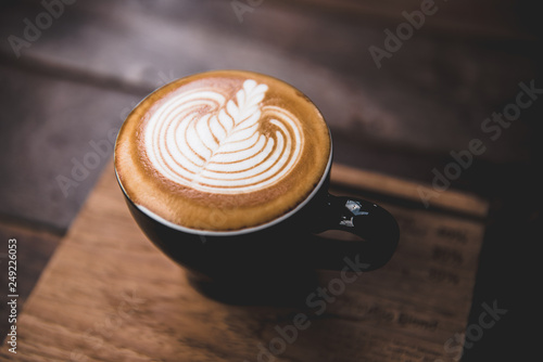 Cup of cappuccino with latte art in black cup with wooden background