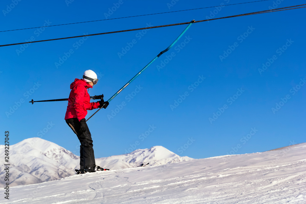 skier in equipment rises on a lift up the hill for skiing against the blue sky and mountain peaks.