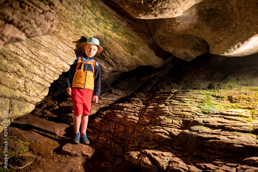 Boy inside the ancient cave with stone walls with additional lighting. Texture of a stone wall in a cave.