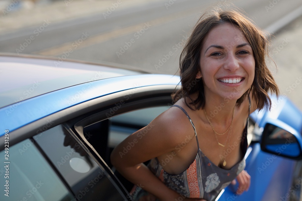 Happy young woman smiling while hanging out of car window 