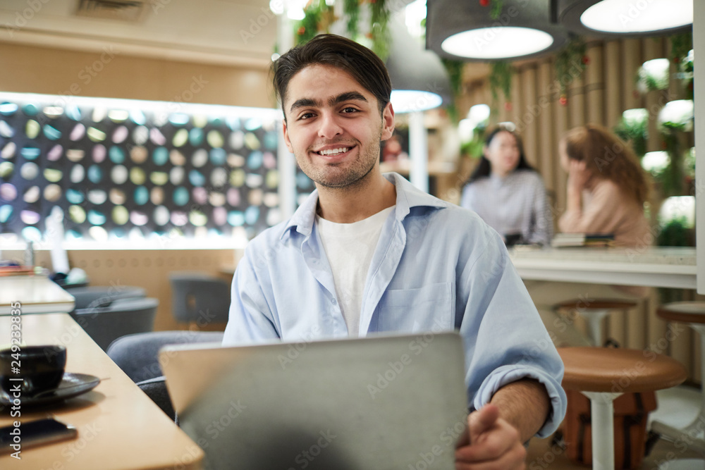Happy casual teenage student looking at you while preparing for lesson or seminar in college cafe Happy casual teenage student looking at you while preparing for lesson or seminar in college cafe