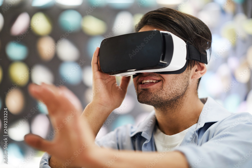 Young happy man in vr goggle enjoying virtual travel and touching new three dimension reality Young happy man in vr goggle enjoying virtual travel and touching new three dimension reality