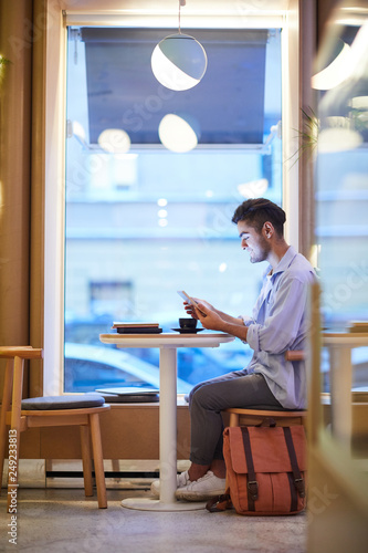 Casual guy with touchpad sitting by table in cozy cafe at lesire, having tea, resting and watching online video