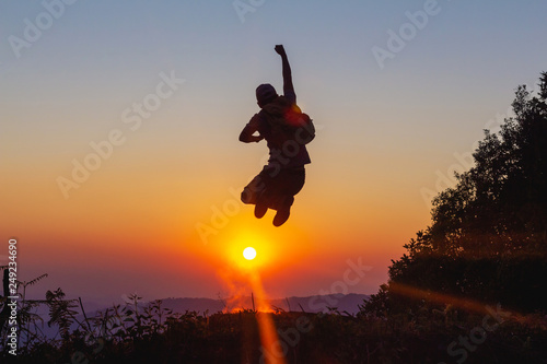 Silhouette of happy hiker man jumping on mountain at sunset time