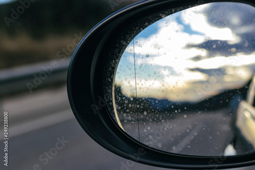 Bright cloudscape reflecting on an oval black mirror car while driving on a highway