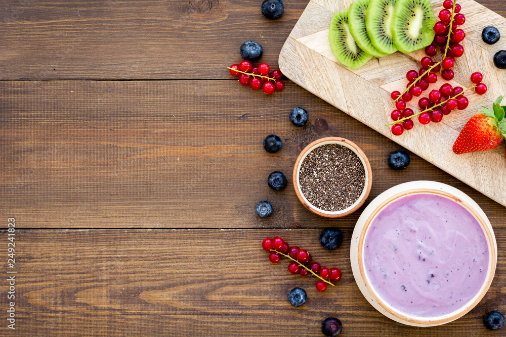 Cook trendy breakfast. Acai smoothie bowl near cutting board with fresh fruits, berries, chia seeds on dark wooden background top view copy space Cook trendy breakfast. Acai smoothie bowl near cutting board with fresh fruits, berries, chia seeds on dark wooden background top view copy space