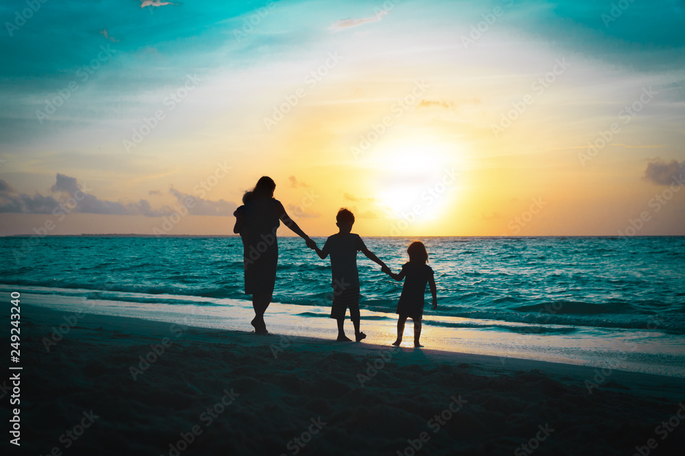 mother with kids walking on beach at sunset
