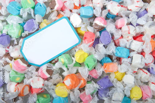 Background of salt water taffy in various flavors and colors wrapped in white transparent paper, blank card on top. Salt water taffy is sold widely on the boardwalks in the U.S. and Canada. photo