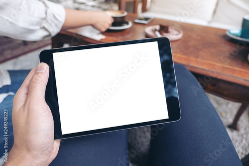 Mockup image of a man's hands holding black tablet pc with blank white screen horizontally while sitting in cafe