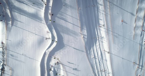 Aerial - Top down static shot of ski area in the winter resort. People skiing fast down the slope on a sunny winter day. Skiers and snowboarders