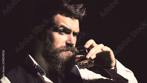 Man with beard holds glass brandy. Bearded drink cognac. Sommelier tastes drink. Man holding a glass of whisky. Sipping whiskey. Portrait of man with thick beard. Macho drinking. Degustation, tasting photo