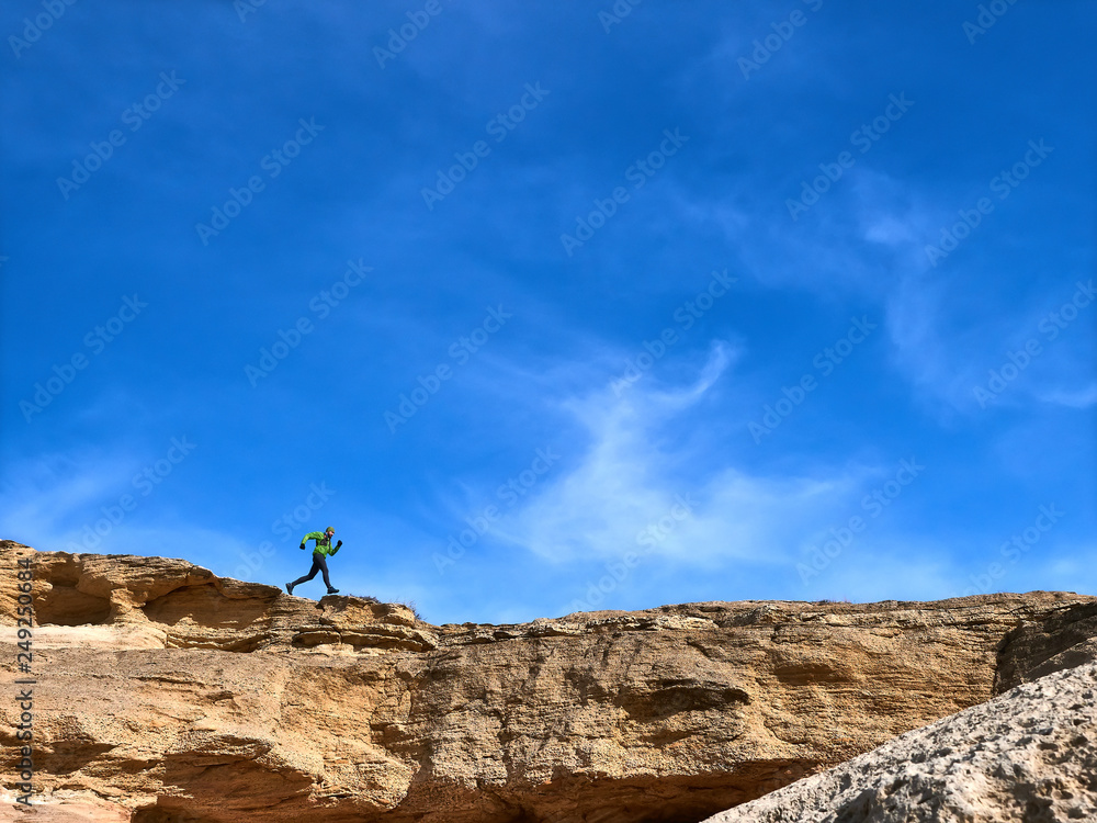 The athlete runs along the edge of a cliff against the sky. Trail Running