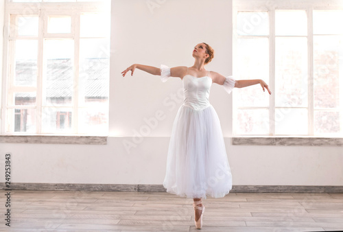Young graceful ballerina dancing on white studio.