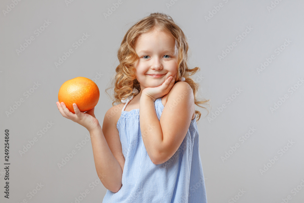 Happy little girl child holding a grapefruit. Healthy food. Gray background, studio, portrait Happy little girl child holding a grapefruit. Healthy food. Gray background, studio, portrait