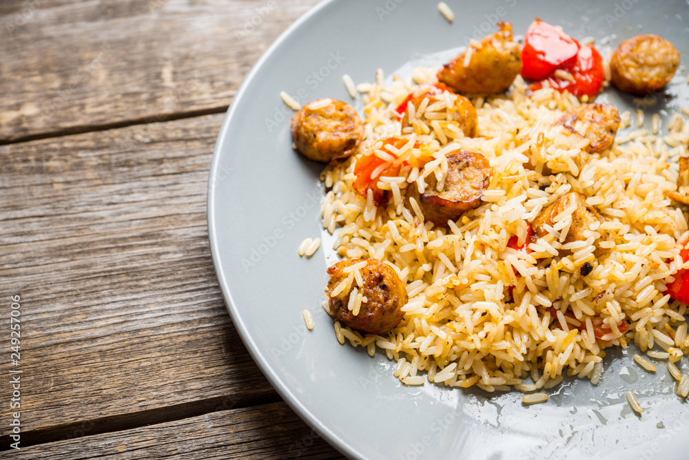 Roasted rice with grilled sausages and bell pepper on the wooden table. Selective focus. Shallow depth of field. Roasted rice with grilled sausages and bell pepper on the wooden table. Selective focus. Shallow depth of field.