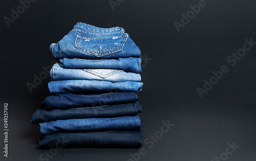 Stack of various blue jeans on black background. Beauty and fashion, clothing concept. Detail of nice blue jeans. Jeans texture or denim background. Collection of jeans. photo