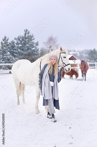 Young happy smiling attractive blond woman with horse, overcast winter day