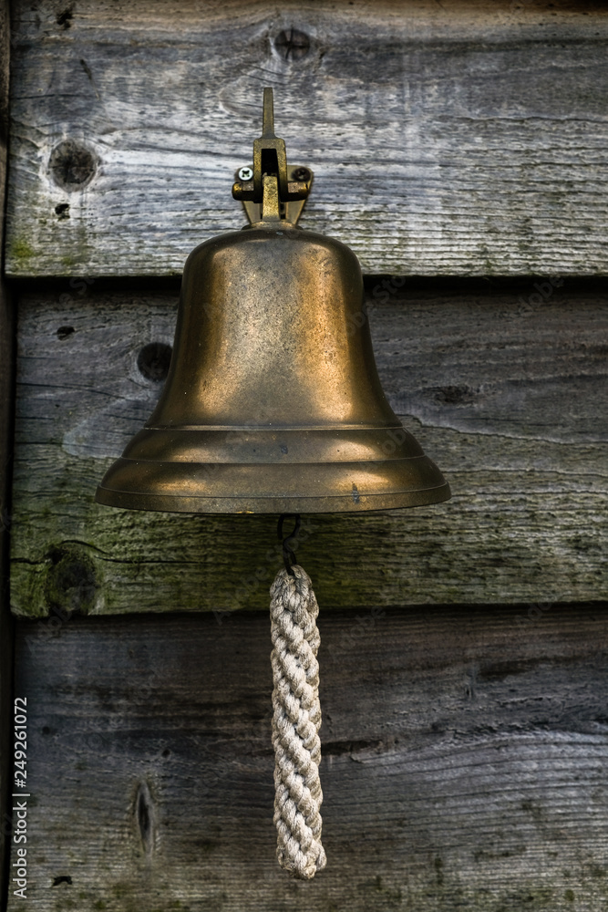 Obraz premium A close up of a small ships bell with a white lanyard hanging outside a house