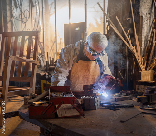 A senior white-haired man in his DIY shop soldering metal parts