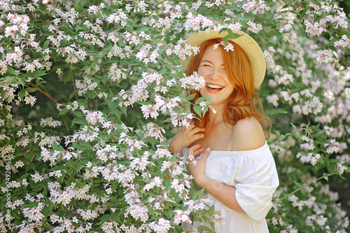 Adult beautiful red-haired woman poses at a blooming jasmine bush.