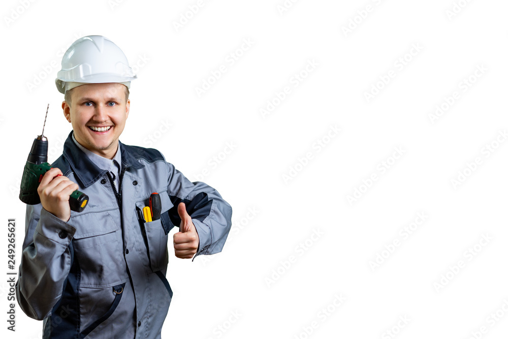 Portrait of handsome attractive repairer in protective white hard hat, overalls, shirt showing having equipment in arm isolated on background Portrait of handsome attractive repairer in protective white hard hat, overalls, shirt showing having equipment in arm isolated on background