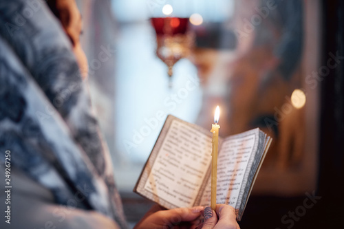 woman in the Russian Orthodox Church with red hair and a scarf on her head lights a candle and prays in front of the icon.