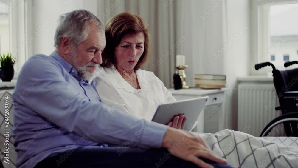 A senior couple with tablet at home, a husband spending time with his ill wife. A senior couple with tablet at home, a husband spending time with his ill wife.
