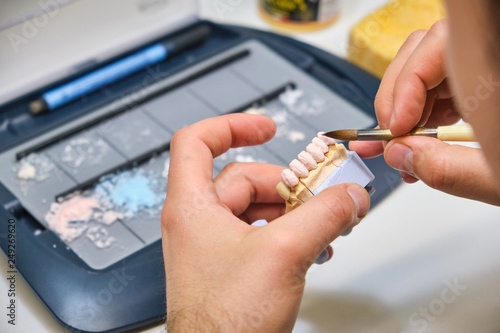 Technician dental is working with complete lower and upper metal ceramic prosthesis dental. Dental technician works by brush with jaw model