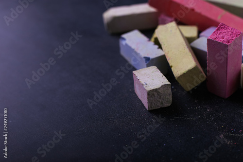 Multicolored crayons lie on a black chalkboard, copy space, macro. The concept of school, education and childhood.