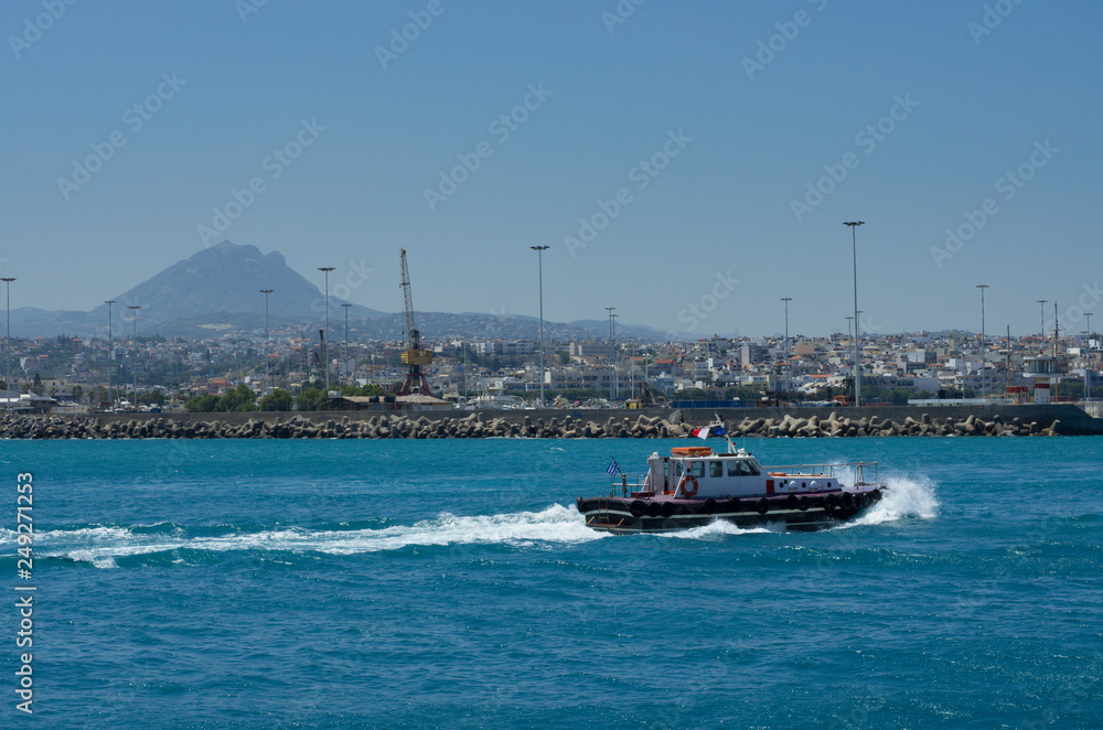 Pilot boat sailing on the azure sea in the Harbor of Heraklion on the background of the mountain top and the city (Greece)
