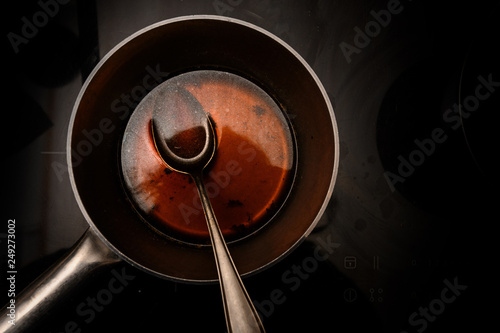 Fotografi pot and spoon with beef stock while cooking a red wine morel sauce on a black st
