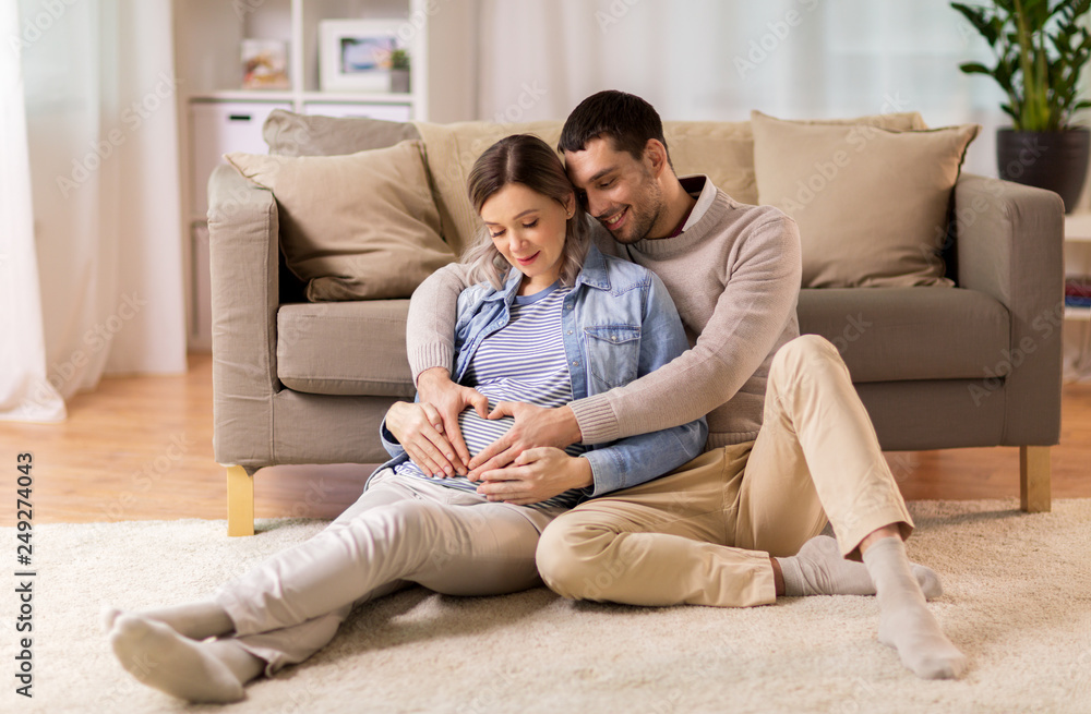 pregnancy, love and care concept - happy man hugging pregnant woman and making hand heart gesture at home pregnancy, love and care concept - happy man hugging pregnant woman and making hand heart gesture at home
