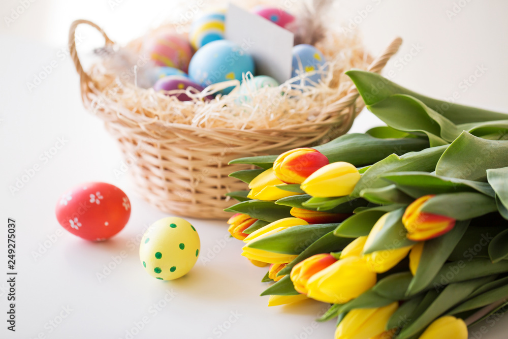 easter, holidays, tradition and object concept - close up of colored eggs in basket and tulip flowers on white background easter, holidays, tradition and object concept - close up of colored eggs in basket and tulip flowers on white background
