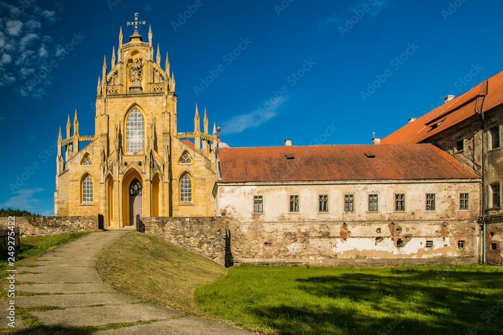 Kladruby, Czech Republic / Europe - July 7 2018: Church of the Assumption of the Virgin Mary built in baroque gothic style,  historical stone buildings with red roofs, sunny day, blue sky, green grass
