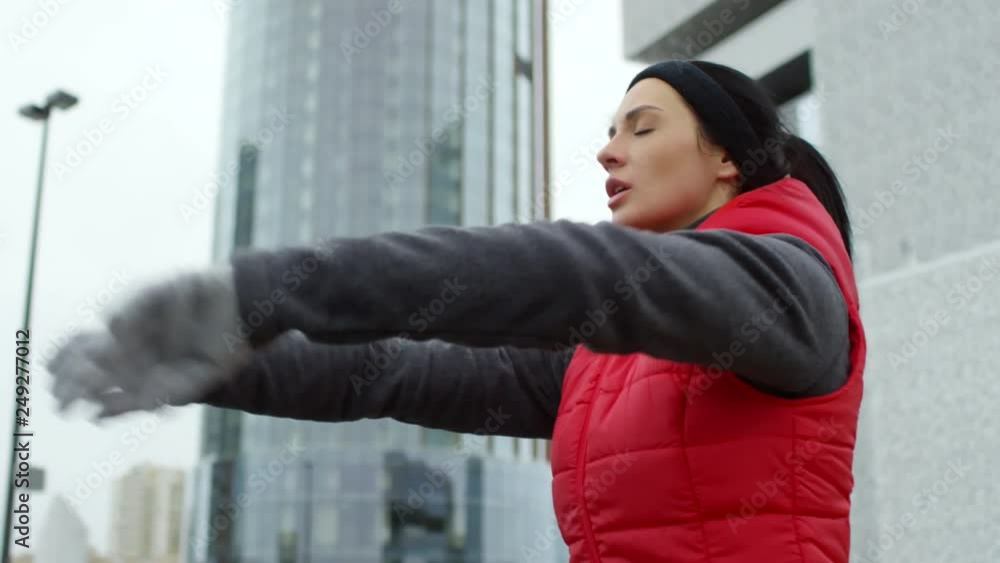 Medium shot of determined young female athlete in sports clothes warming up before outdoor workout Medium shot of determined young female athlete in sports clothes warming up before outdoor workout