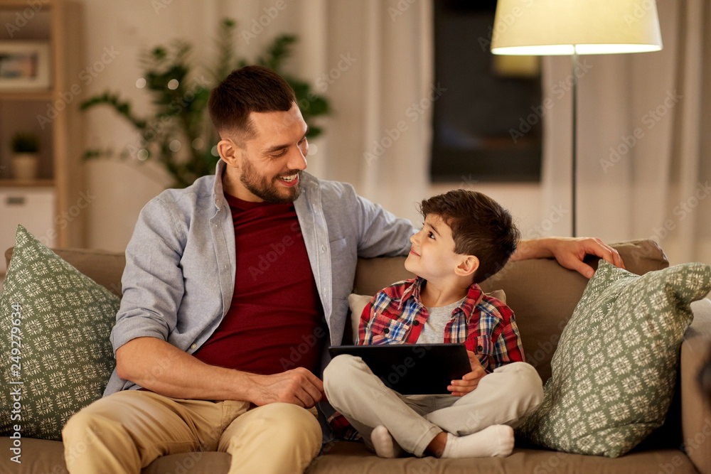 family, fatherhood, technology and people concept - happy father and little son with tablet pc computer sitting on sofa at home in evening family, fatherhood, technology and people concept - happy father and little son with tablet pc computer sitting on sofa at home in evening
