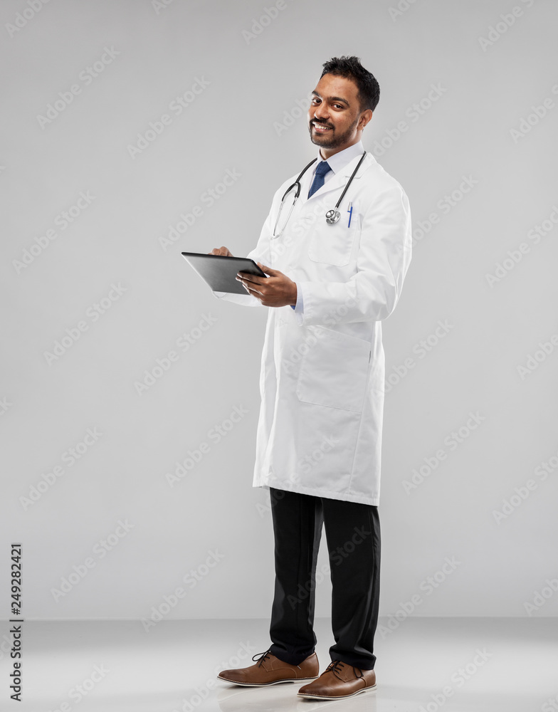 medicine, technology and healthcare concept - smiling indian male doctor in white coat with tablet computer and stethoscope over grey background medicine, technology and healthcare concept - smiling indian male doctor in white coat with tablet computer and stethoscope over grey background
